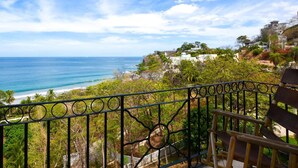 Uma varanda com vista para o oceano e uma colina com edifícios.