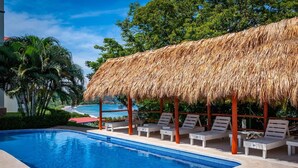 Uma piscina com espreguiçadeiras e uma estrutura de telhado de palha.