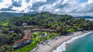 Un complejo turístico en la costa con playa, piscina y abundante vegetación.