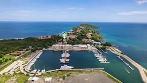 Vista aérea de uma marina com barcos atracados, um prédio da marina e uma pequena ilha com edifícios.