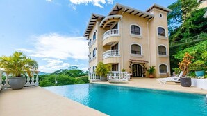 Um edifício com vários andares, piscina, varandas e plantas em vasos.