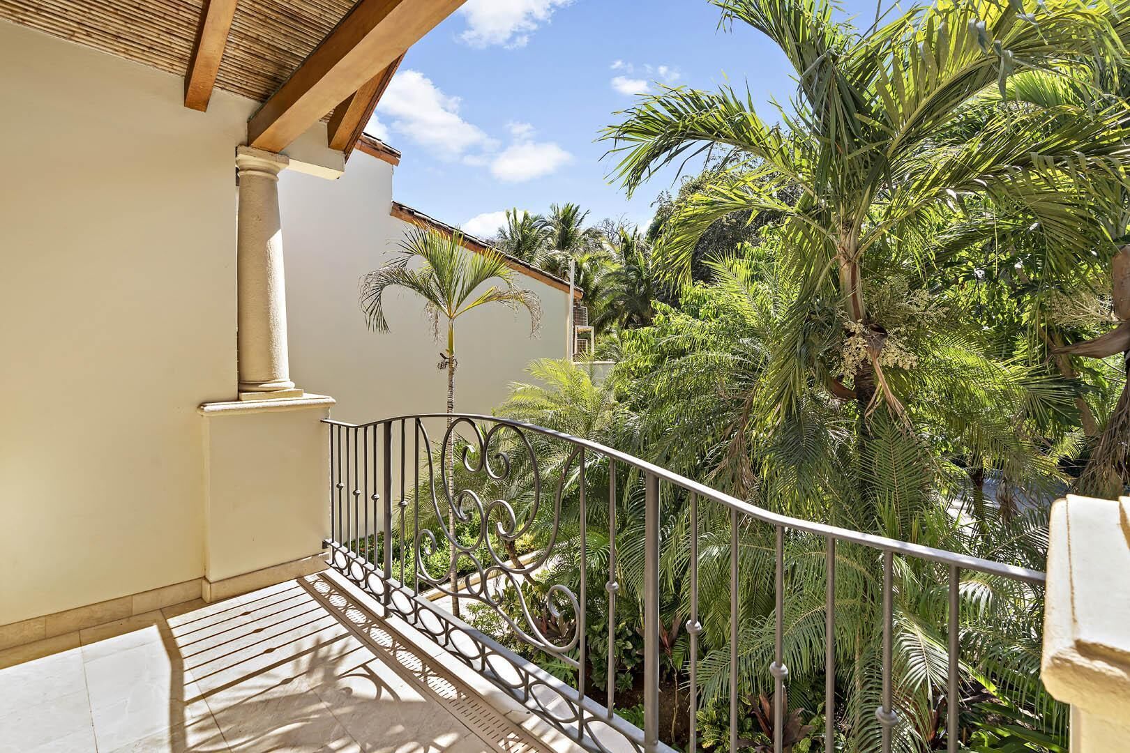 Un balcon doté d’une balustrade en fer forgé, donnant sur un jardin luxuriant planté de palmiers.