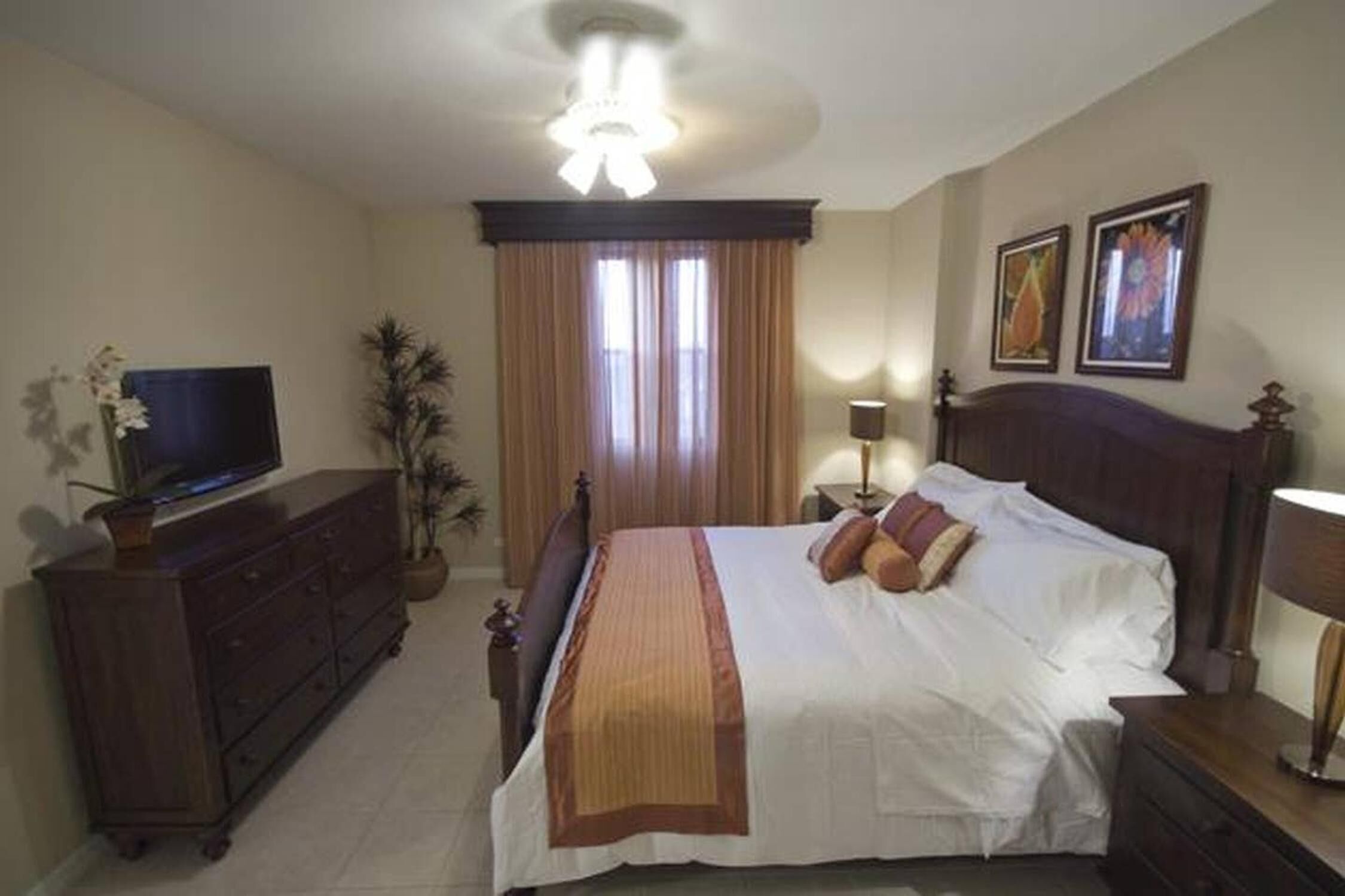 Une chambre d’hôtel avec un grand lit, un téléviseur posé sur une commode, une lampe et une fenêtre avec des rideaux.