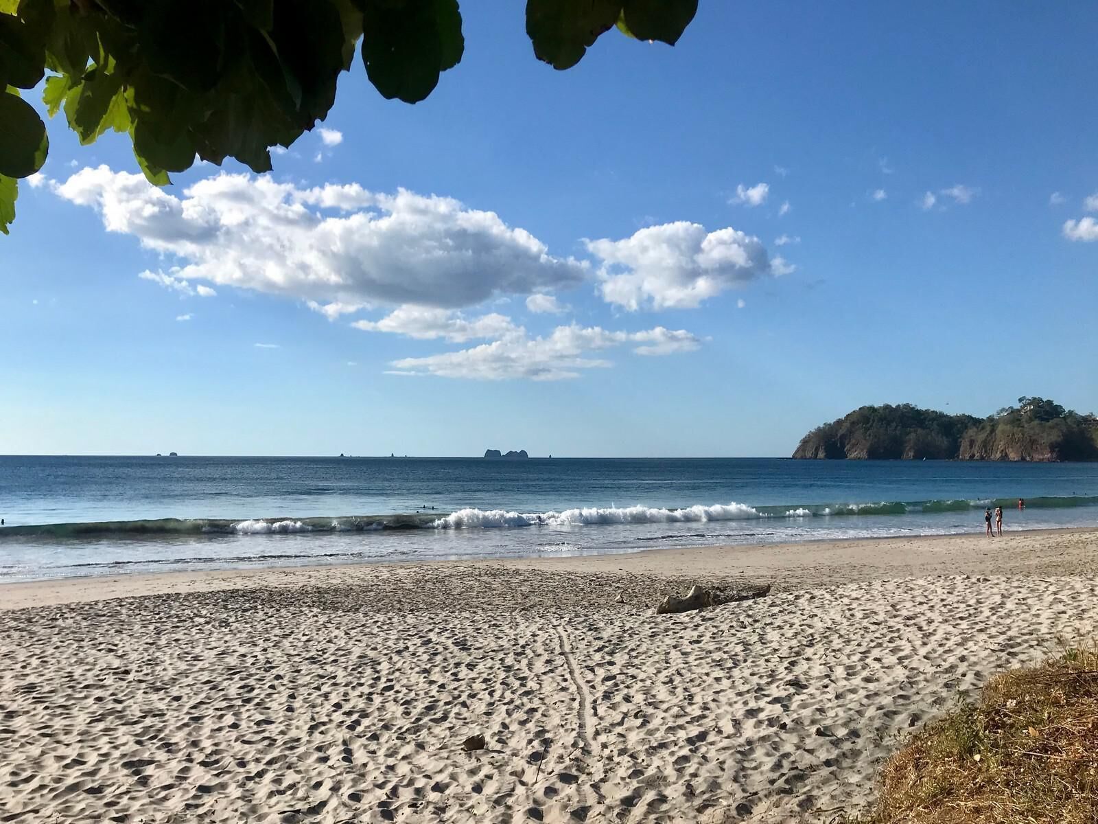 Une plage avec un ciel dégagé et des vagues calmes, un rivage sablonneux et un promontoire rocheux situé au loin.
