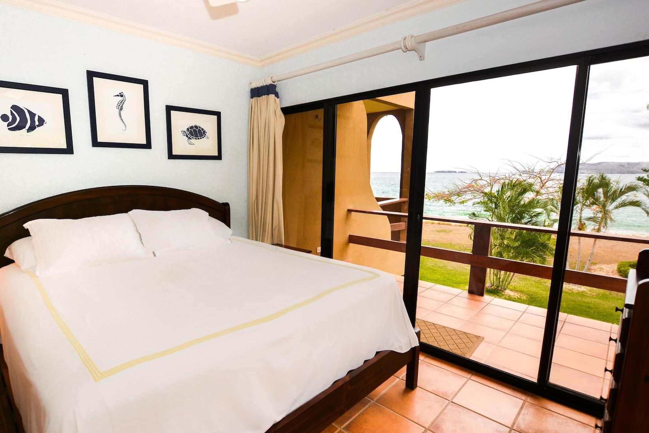 Une chambre d’hôtel avec un lit, un balcon donnant sur la mer et des tableaux encadrés accrochés au mur.