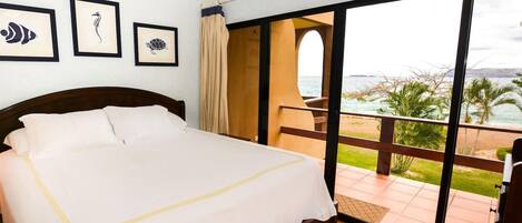 A hotel room with a bed, a balcony with a view of the sea, and framed pictures on the wall.