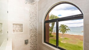 Une salle de bain dotée d’une grande fenêtre donnant sur une plage et des palmiers.
