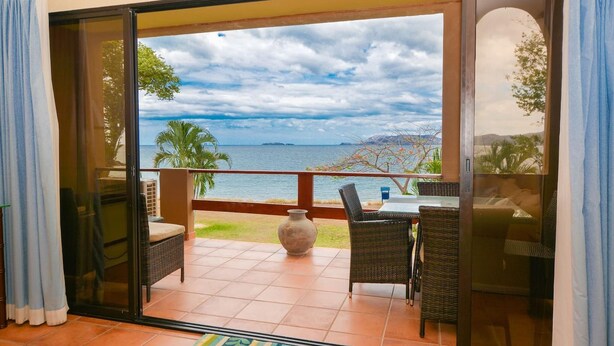 Un balcon avec vue sur la mer, des meubles en osier et un sol carrelé.