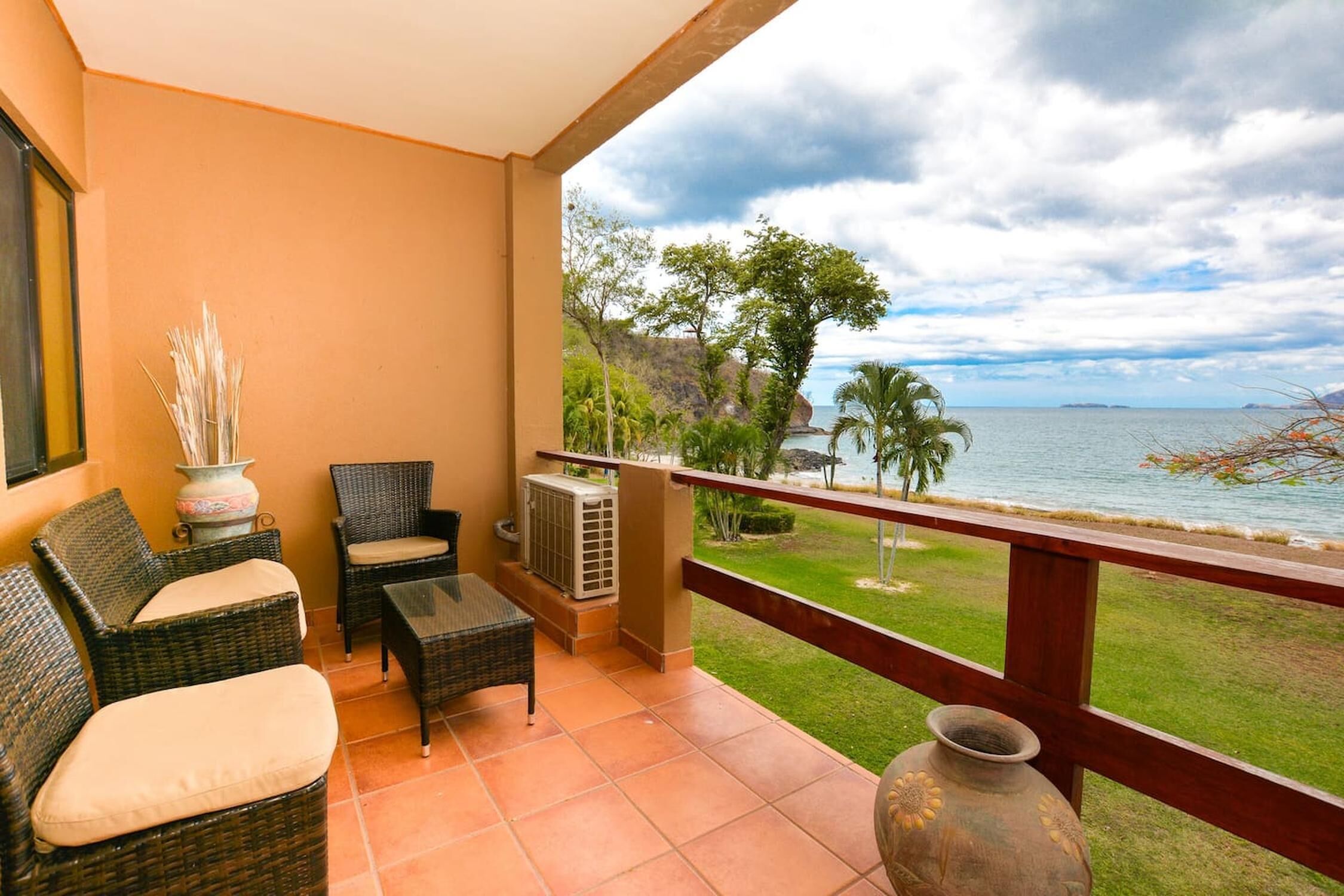 Ein Balkon mit Korbmöbeln, einer Vase und Blick auf das Meer und die grüne Landschaft.