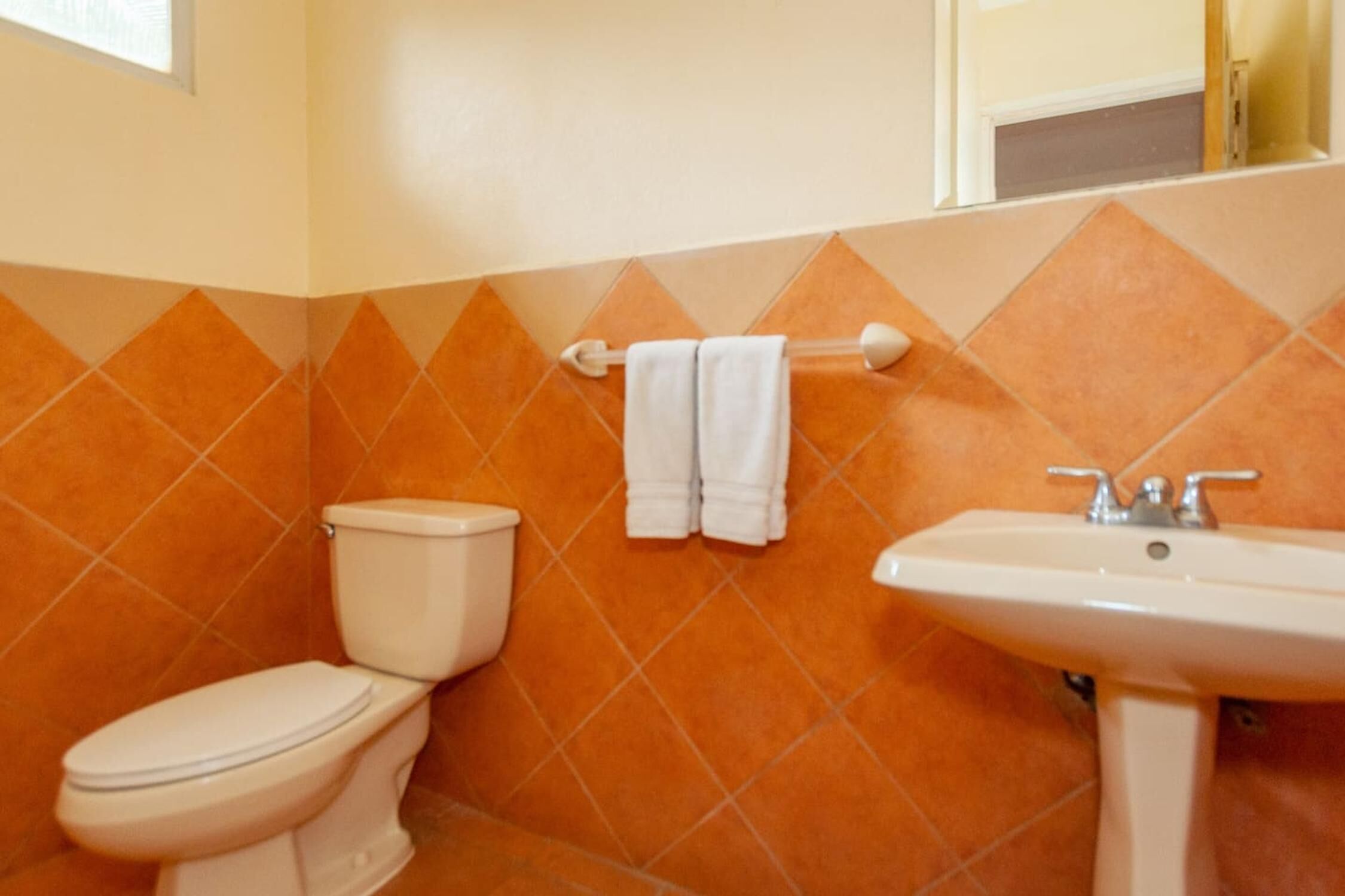A bathroom with a toilet, sink, and orange-tiled walls.