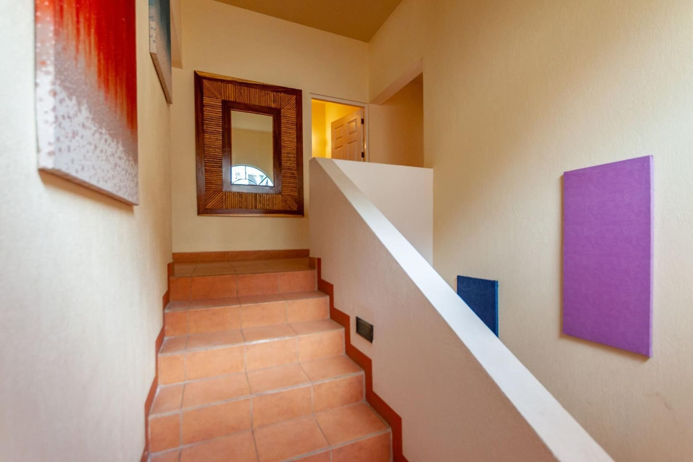 Eine Treppe mit Terrakottafliesen und weißen Wänden, die zu einer Tür führt.