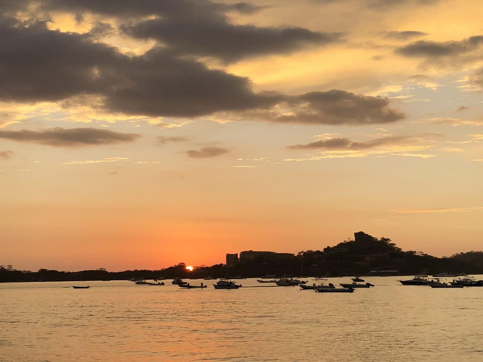 Un coucher de soleil sur une étendue d’eau, avec des bateaux et une colline en arrière-plan.