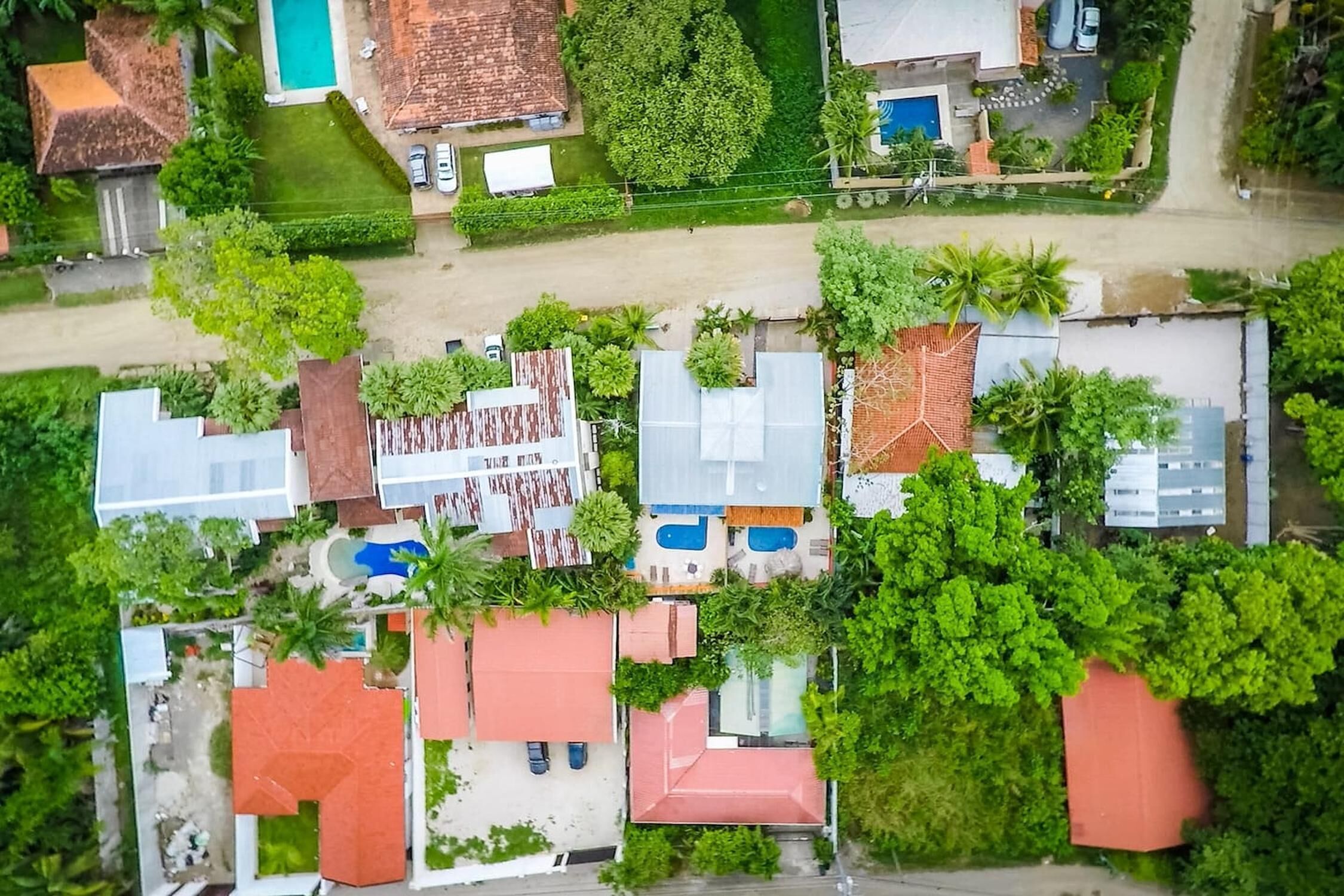 Vue aérienne d’un quartier résidentiel avec de nombreuses maisons, dont certaines sont dotées de piscines, le tout entouré de verdure et de palmiers.