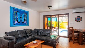 Uma sala de estar com um sofá de couro preto, uma mesa de centro de madeira e um quadro de borboletas coloridas na parede.
