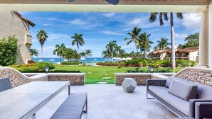 A covered outdoor seating area with a view of the beach and palm trees.
