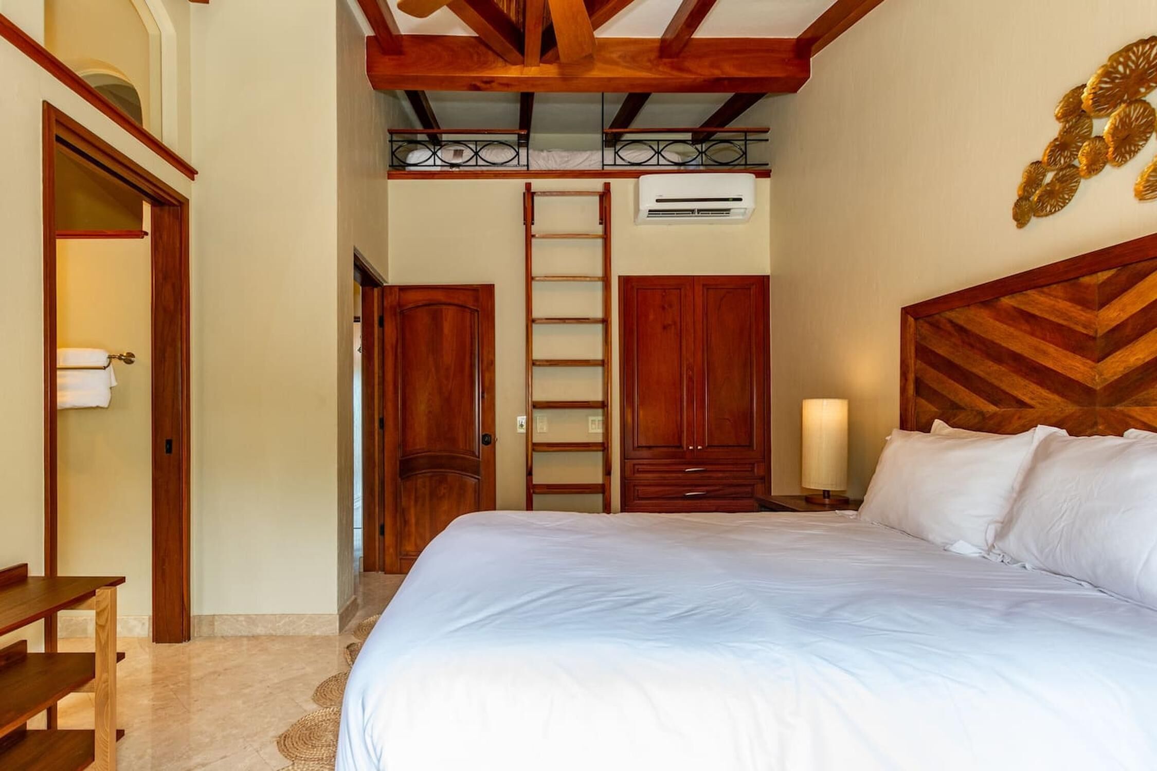 A bedroom with a large bed, wooden wardrobe, a ladder, and a small table.