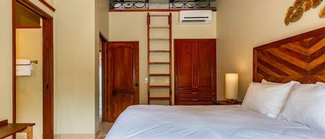 A bedroom with a large bed, wooden wardrobe, a ladder, and a small table.