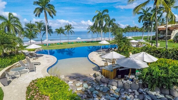 A resort pool with lounge chairs, umbrellas, and a view of the beach.