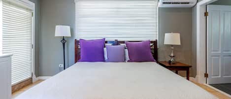 A bedroom with a large bed, two bedside tables, a ceiling fan, and an air conditioning unit.