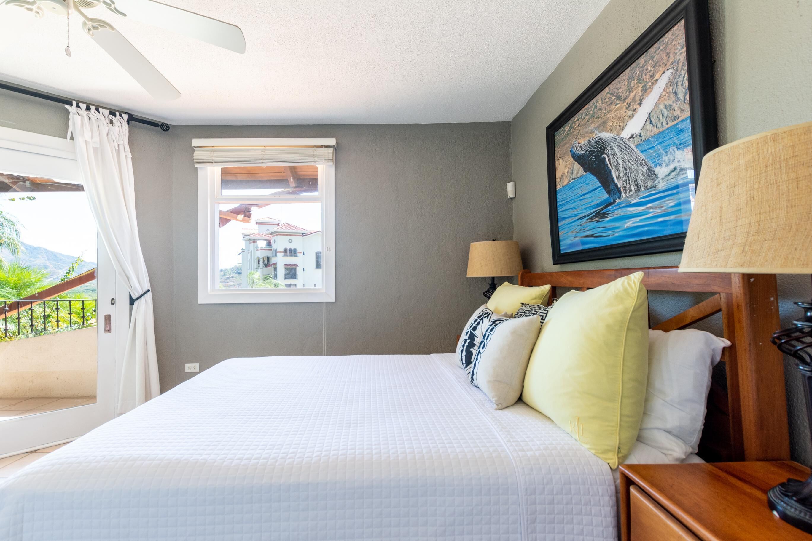 A hotel room with a bed, a window with curtains, a painting of a bear, and a lamp.