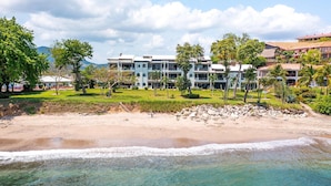 Ett hotell vid stranden med flera byggnader, en sandstrand och kristallklart turkost vatten.