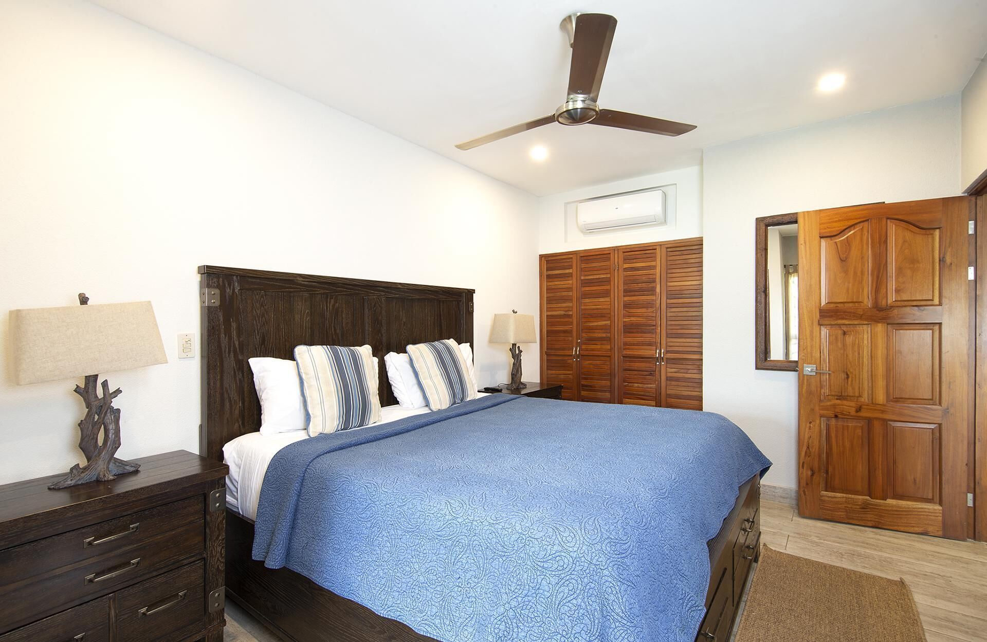 A bedroom with a bed, wooden wardrobe, ceiling fan, and bedside lamps.