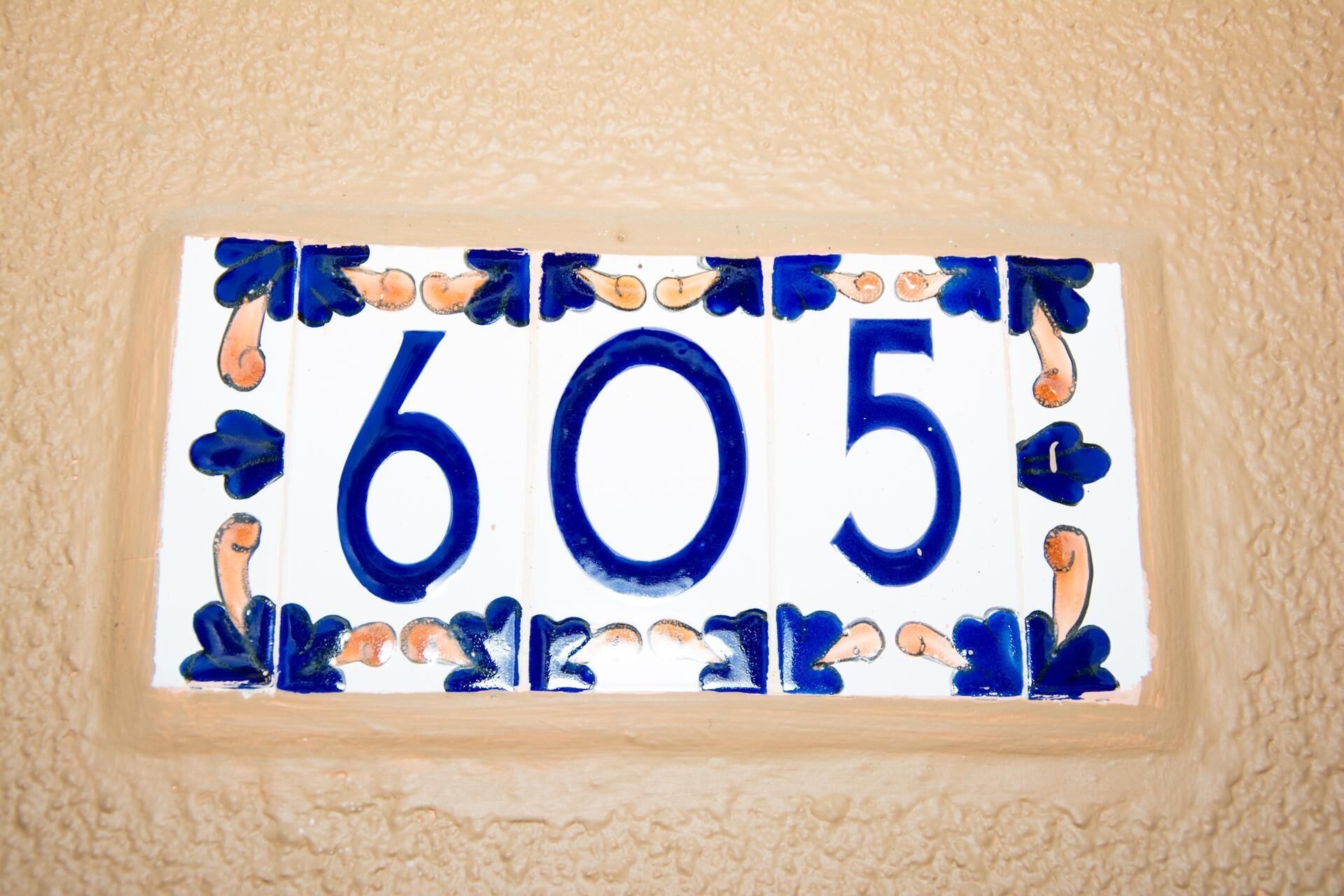 A blue and white house number plaque with the number 605, surrounded by decorative elements.