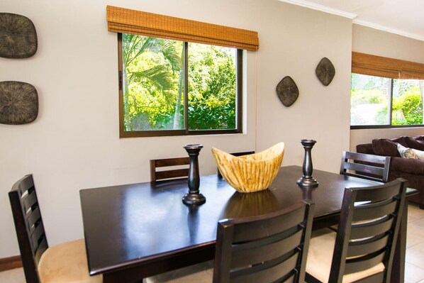 Een eetruimte met een donker houten tafel, vier stoelen, een decoratieve schaal en een raam met uitzicht op groen.