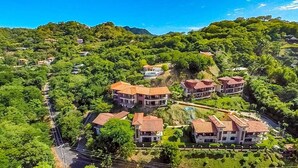 A residential area with multiple houses, some with red-tiled roofs, surrounded by lush greenery and hills. - Stunning Hillside Villa with Panoramic Ocean Views & Infinity Pool (Tempate)