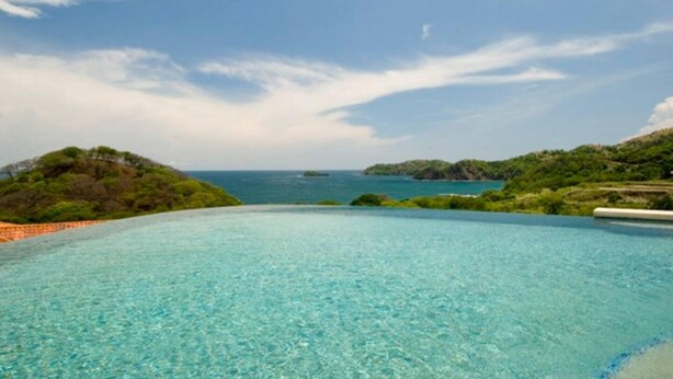 A clear blue infinity pool with a view of the sea and distant islands. - Stunning Hillside Villa with Panoramic Ocean Views & Infinity Pool (Tempate)