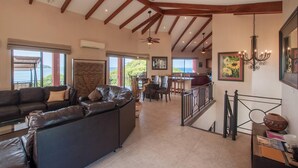 A spacious living area with a leather sofa, a dining table, and a staircase leading to an upper level. - Stunning Hillside Villa with Panoramic Ocean Views & Infinity Pool (Tempate)
