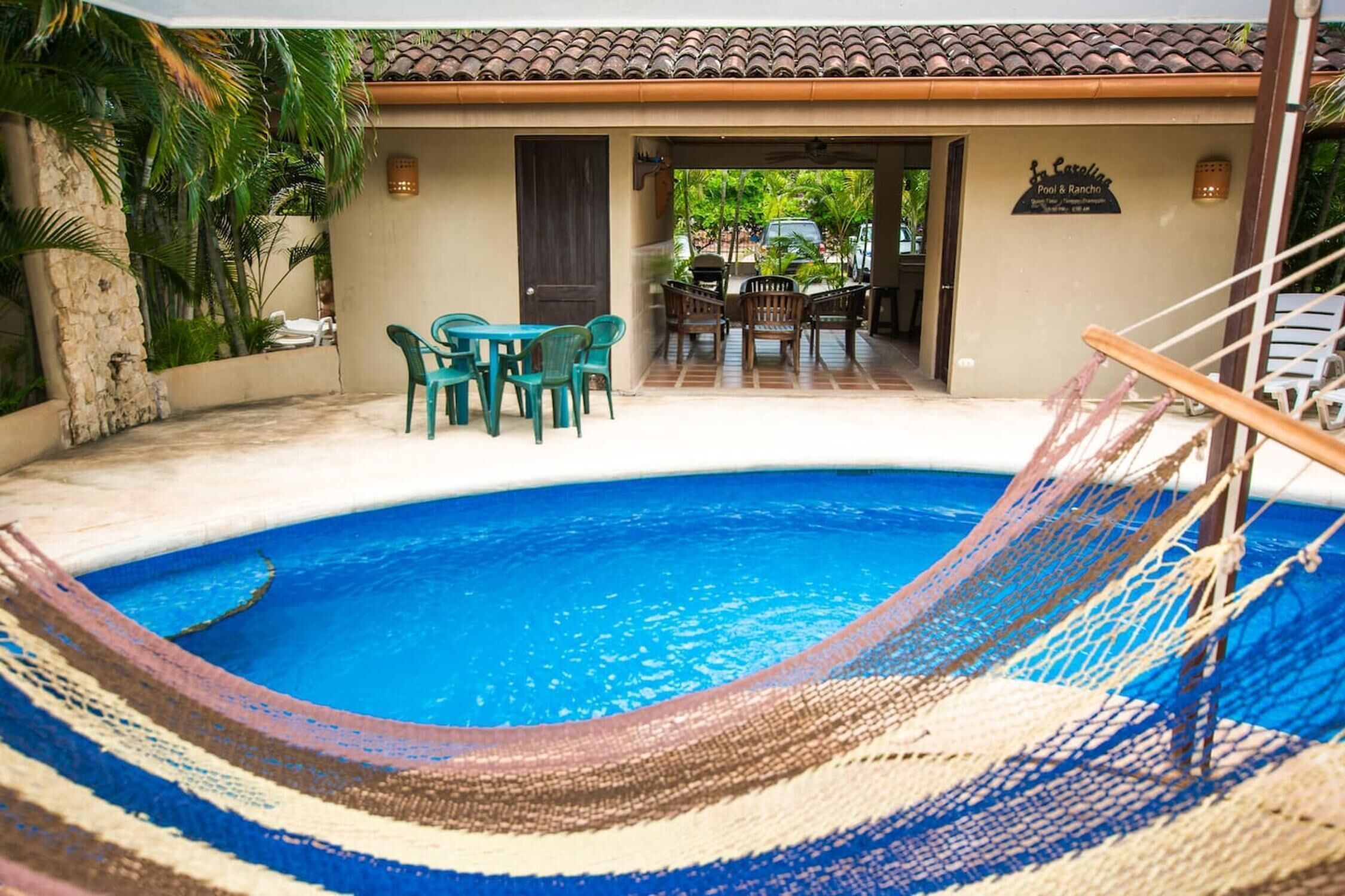 A pool area with a hammock, a dining table with chairs, and a sign for 'La Caracola Pool & Ranch'.
