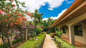 Un chemin mène à un bâtiment qui est bordé d’un côté par un jardin et de l’autre par une clôture.