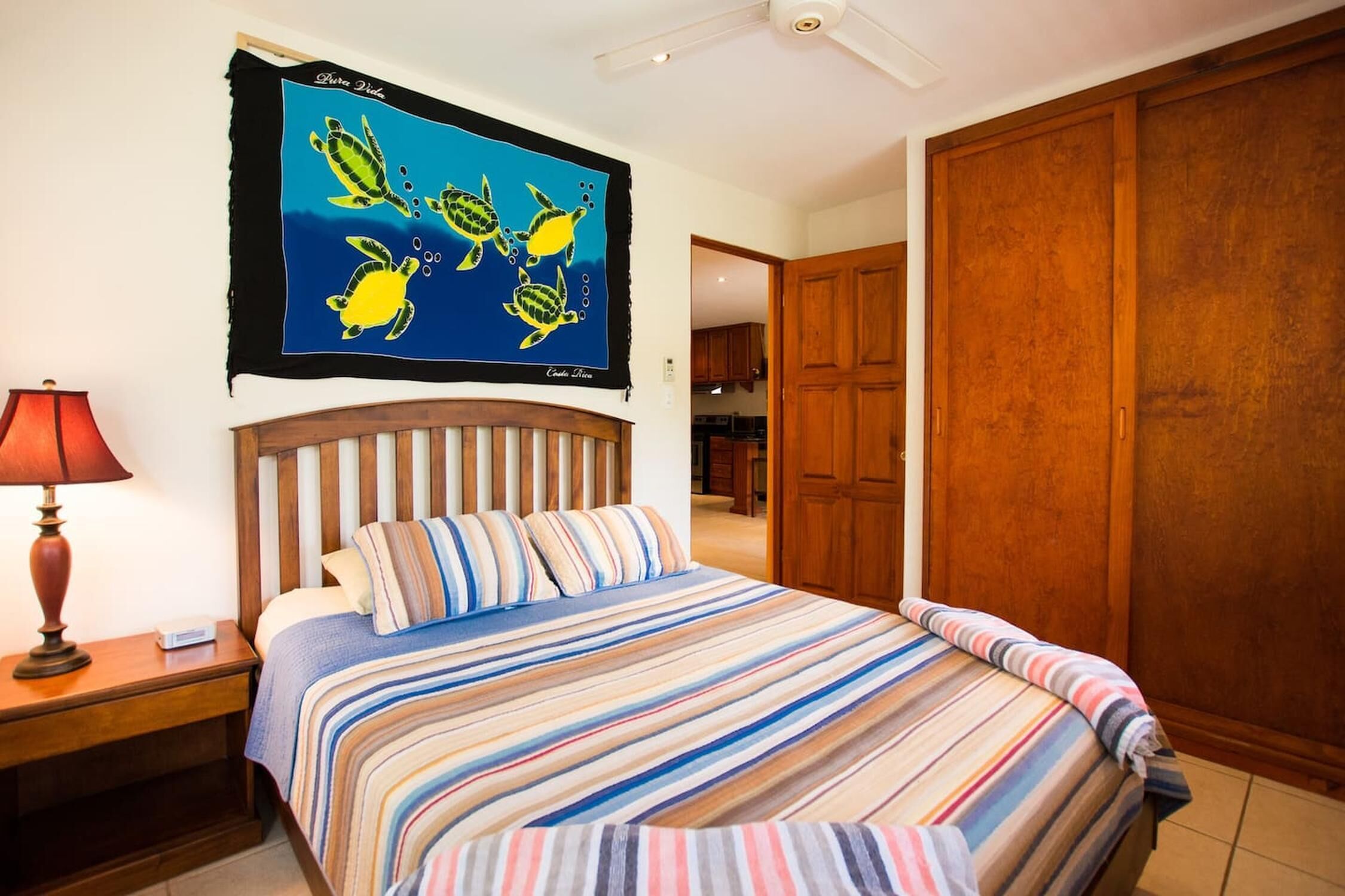 Una camera da letto con copripiumino a righe, una testiera in legno, un comodino con una lampada e un pannello decorativo con tartarughe marine.