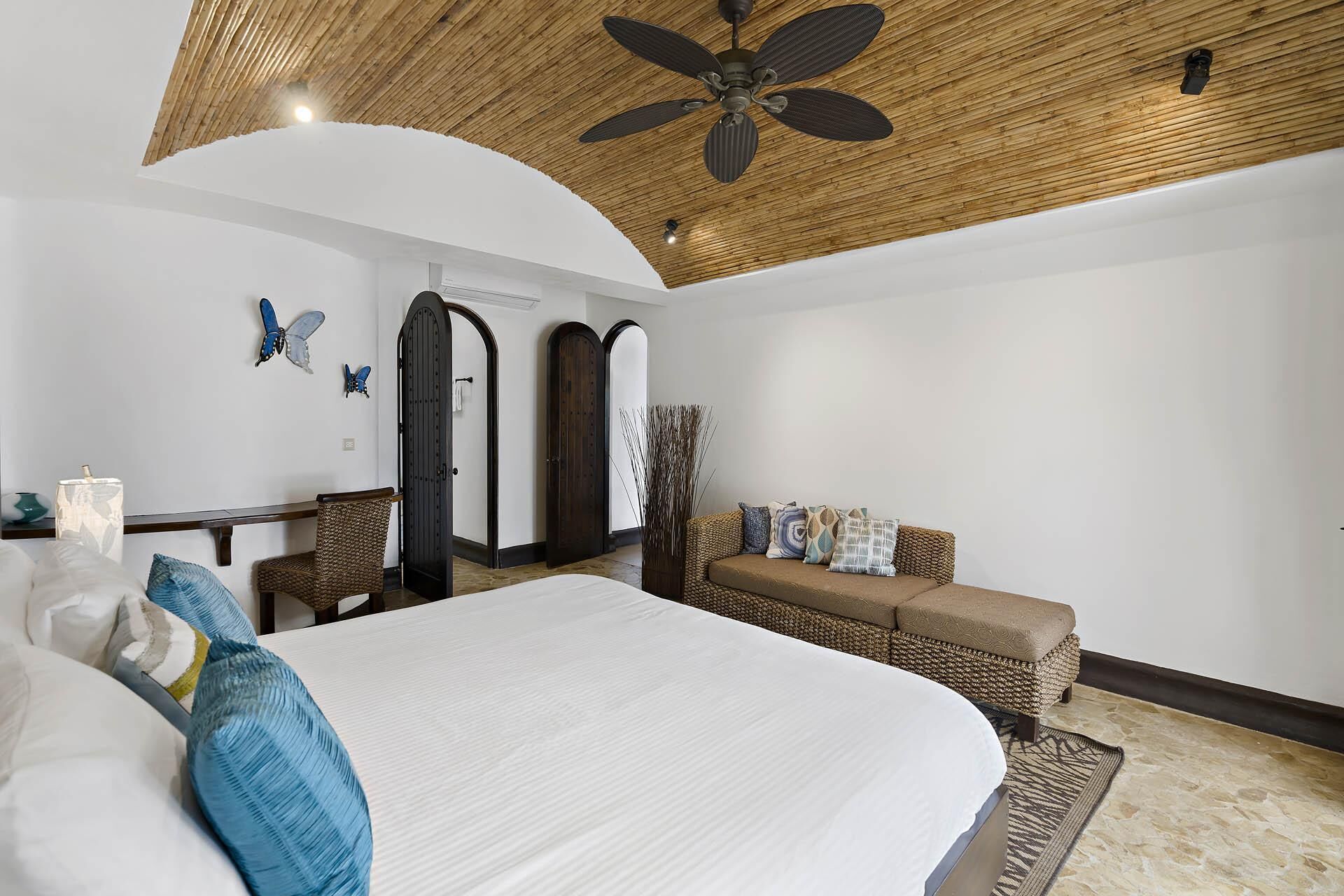 Une chambre avec un grand lit, un ventilateur de plafond en bois, un canapé et un élément décoratif mural.