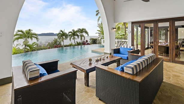 Un espace aménagé au bord de la piscine, avec vue sur la mer, doté de meubles en osier et d’un ventilateur de plafond.