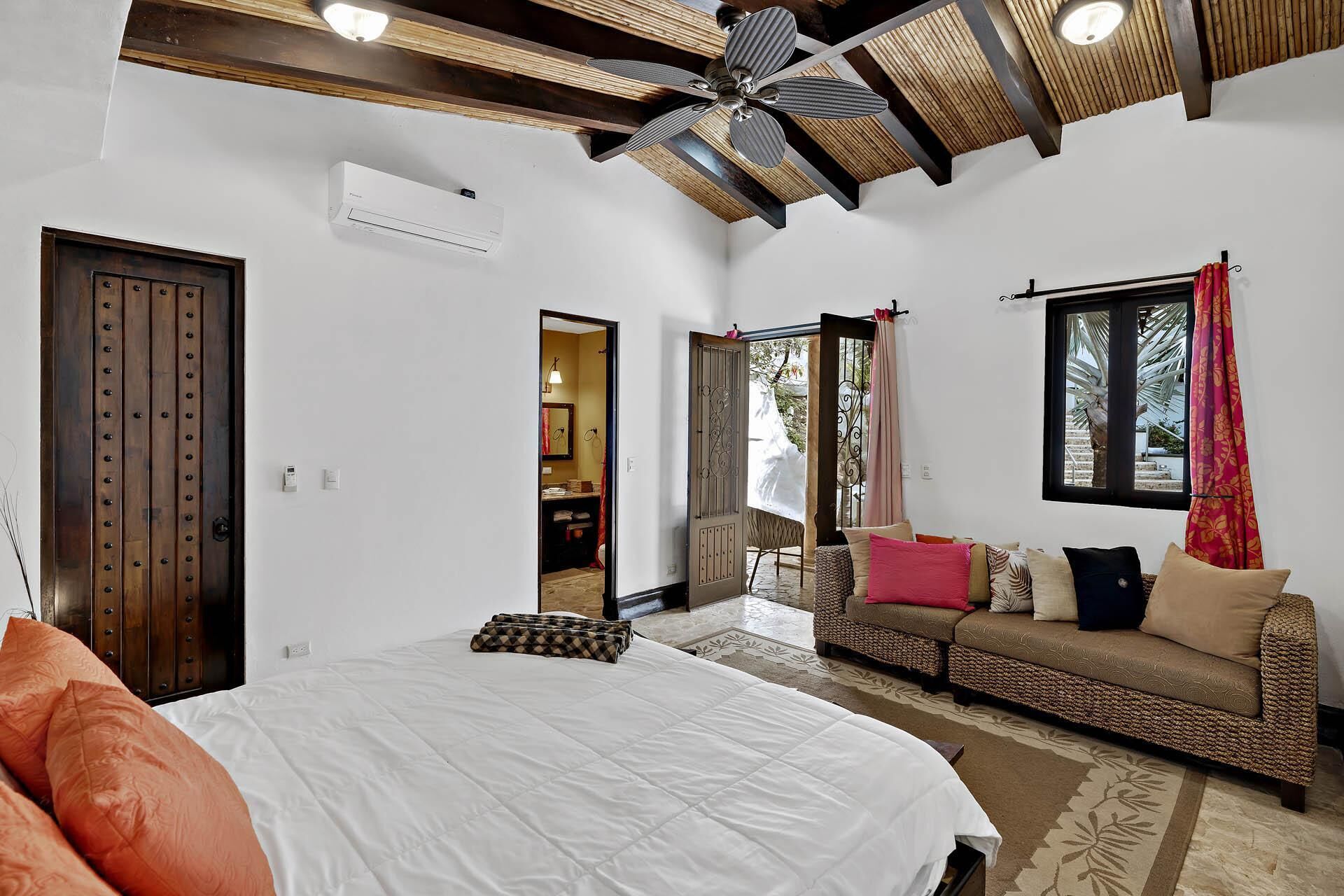 A bedroom with a bed, a sofa, a ceiling fan, and a window.