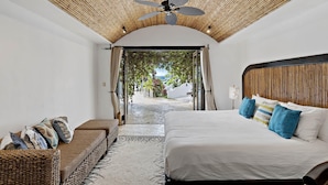 Une chambre avec un lit, un canapé, un ventilateur de plafond et une vue sur un jardin.