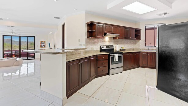 A modern kitchen with dark wood cabinets, a black refrigerator, and a large island with a sink. - Recently Renovated Luxury Condo with Resort-Style Beach Club Access and Ocean Views (Cabo Velas)
