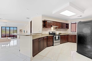 Eine moderne Küche mit dunklen Holzschränken, einem schwarzen Kühlschrank und einer großen Kochinsel mit einer Granit Arbeitsplatte.