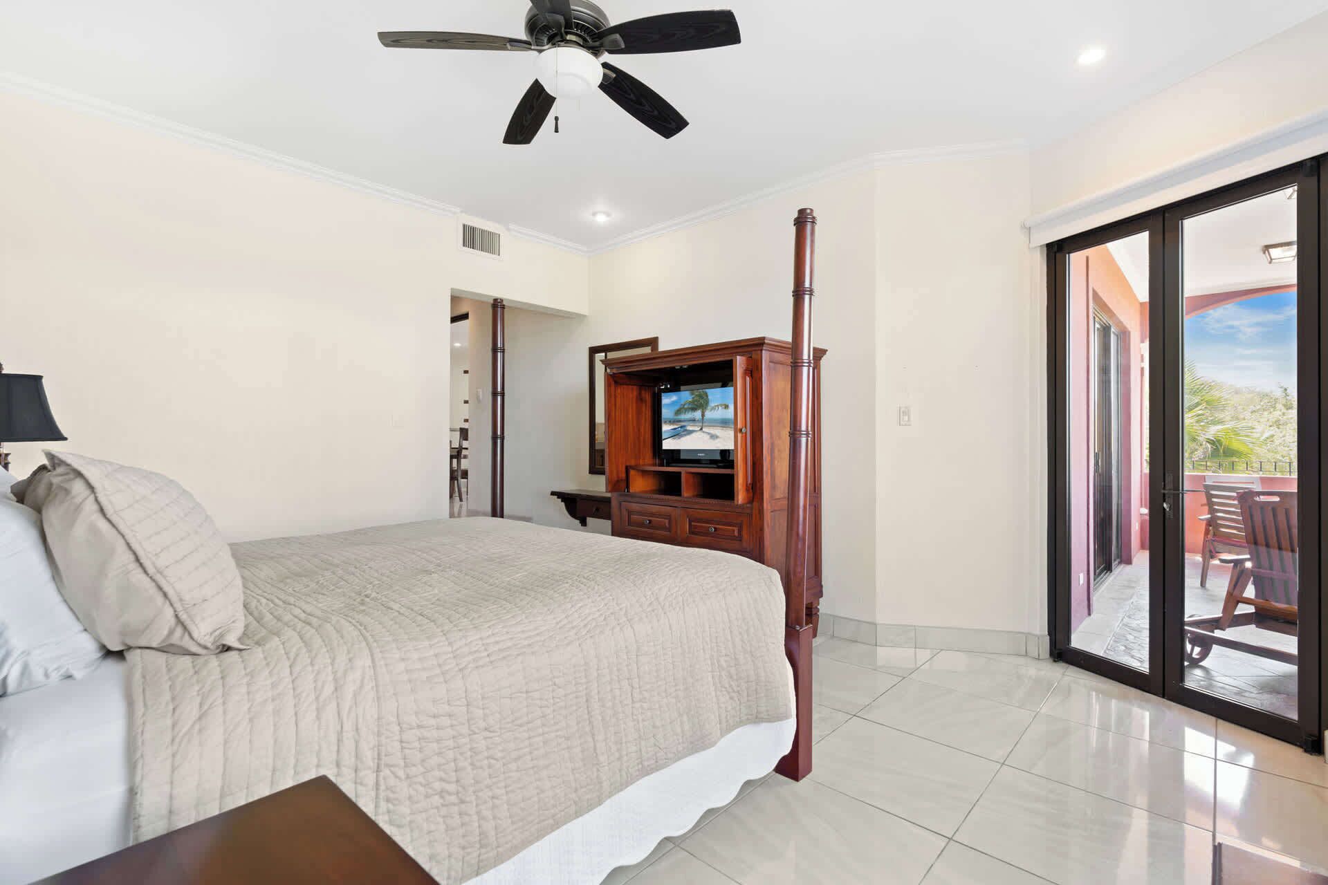 Un dormitorio con cama, televisión, ventilador de techo y puerta corrediza de vidrio que da a un área exterior.