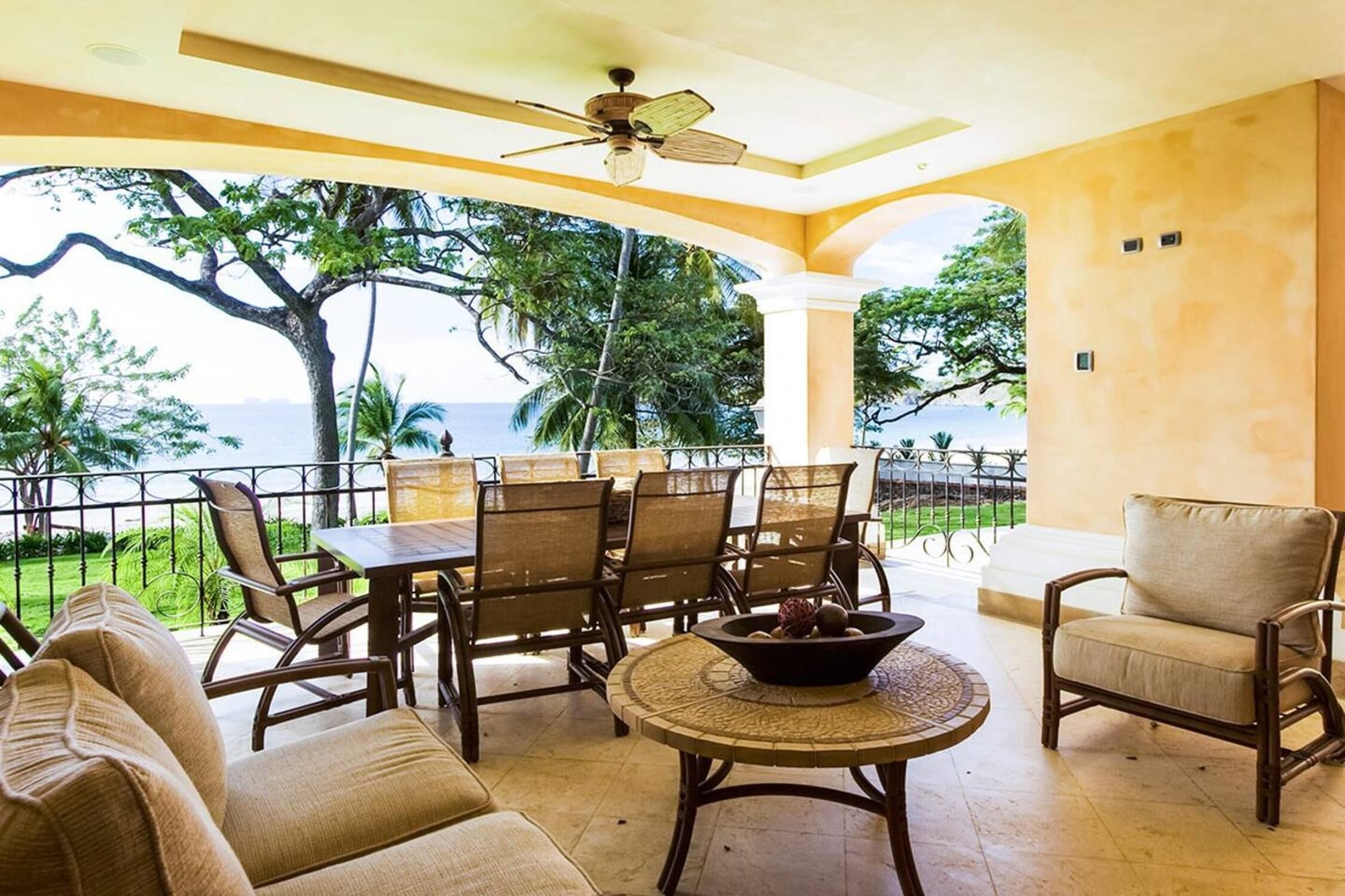 A covered outdoor seating area with a table, chairs, and a bowl of fruit.