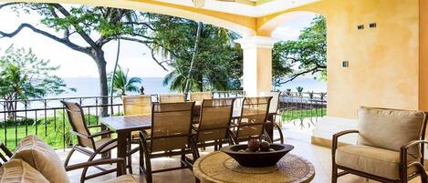 A covered outdoor seating area with a table, chairs, and a bowl of fruit.