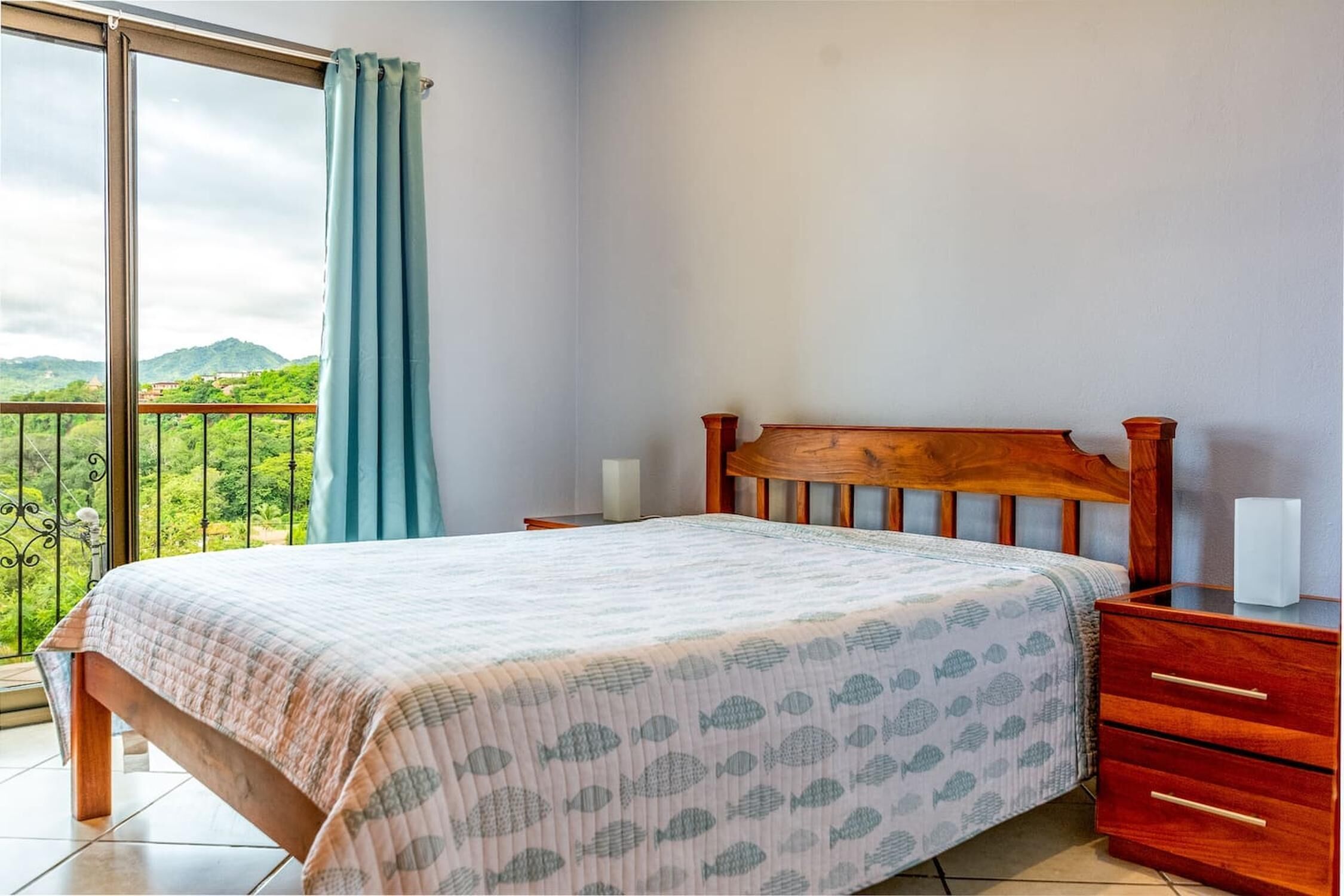 Een slaapkamer met een houten bed, een nachtkastje en uitzicht op groen door een groot raam.