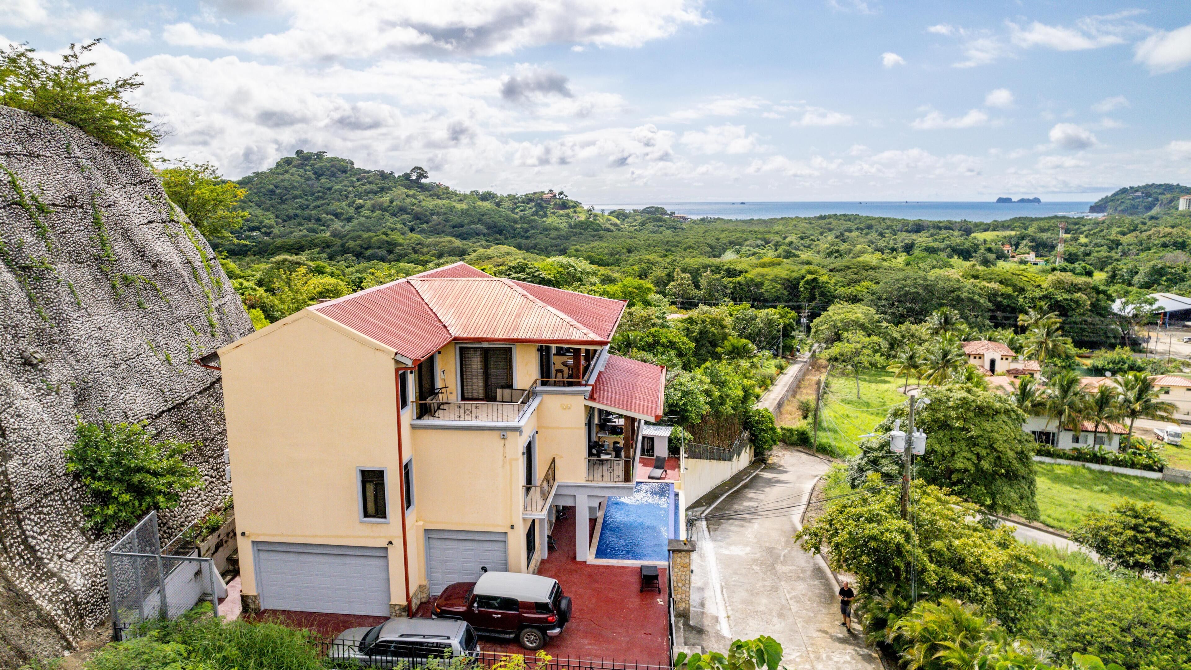 A two-story house with a red roof, a swimming pool, and a view of a lush green landscape.