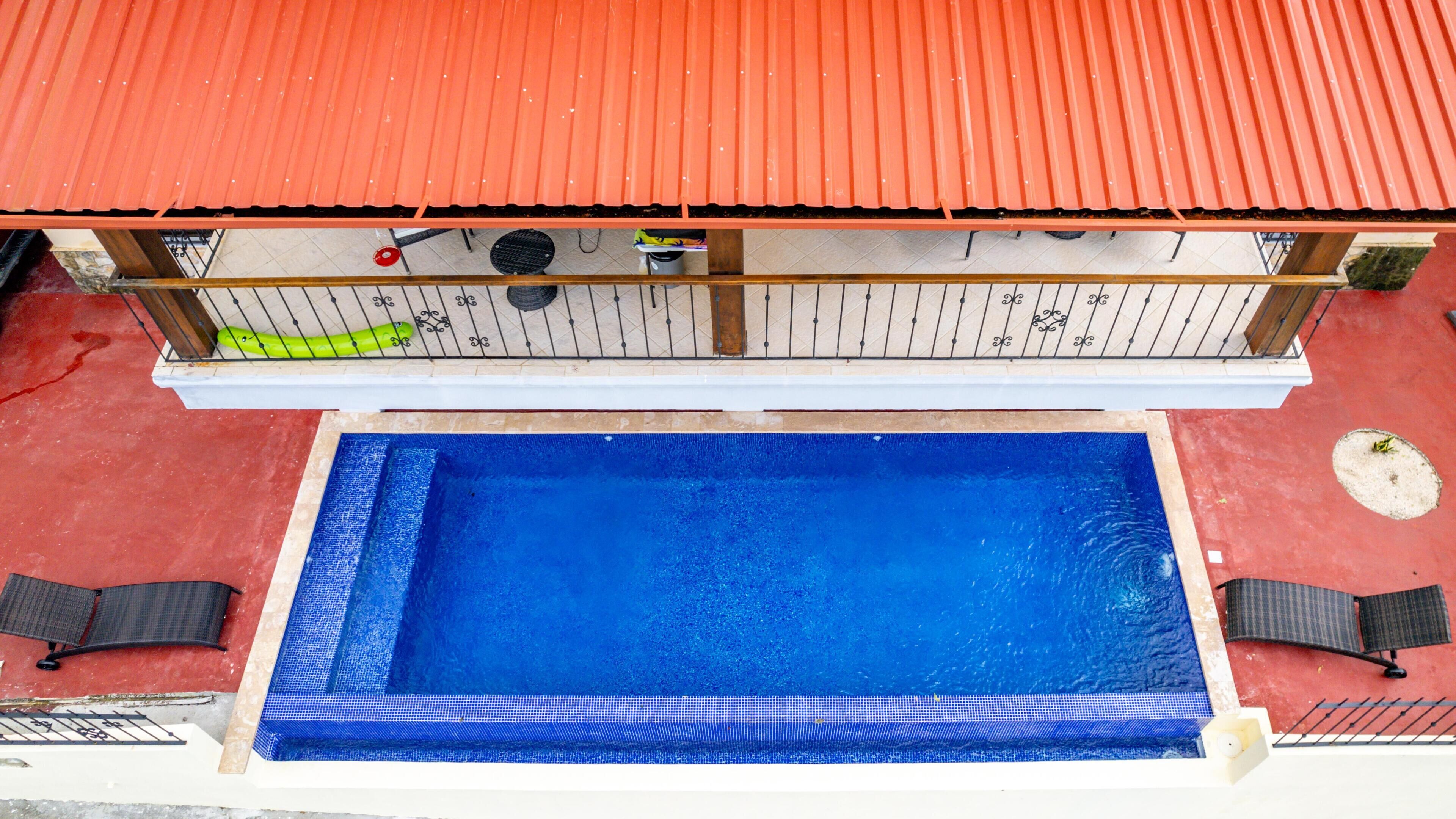 A rooftop pool with a red roof, surrounded by a wooden deck and two black lounge chairs.