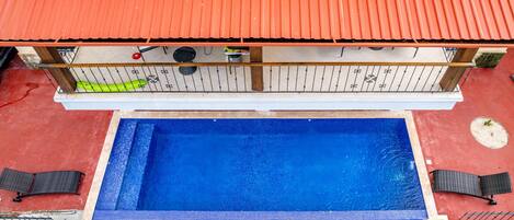 A rooftop pool with a red roof, surrounded by a wooden deck and two black lounge chairs.