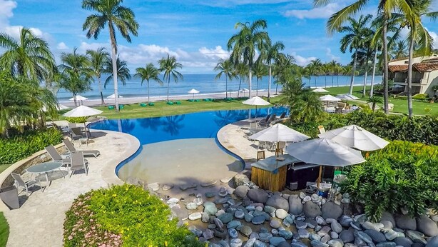 A resort pool area with lounge chairs, umbrellas, and a view of the beach. - Stylish Split-Level Condo with a Shaded Terrace, Direct Beach Access, and Resort-Style Community Amenities (Cabo Velas)