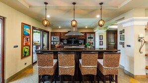 A spacious kitchen with a large island, dark wooden cabinets, stainless steel appliances, and a modern pendant light fixture. - Stunning Luxury Mansion in Playa Flamingo with Six Bedrooms and Beachfront Access (Cabo Velas)