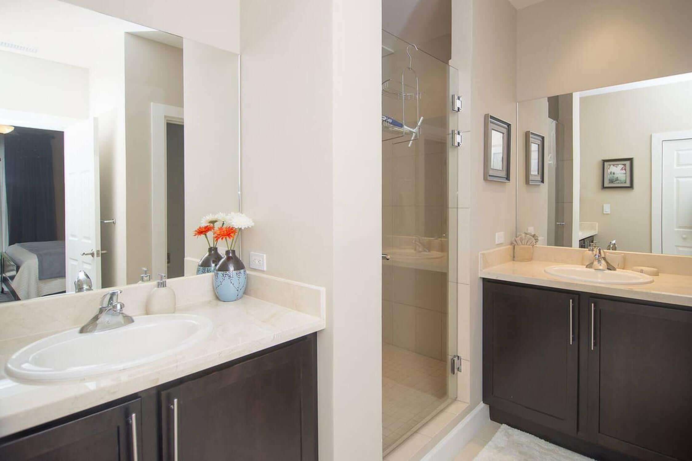Un baño moderno con dos lavamanos, muebles oscuros y mampara de ducha de vidrio.